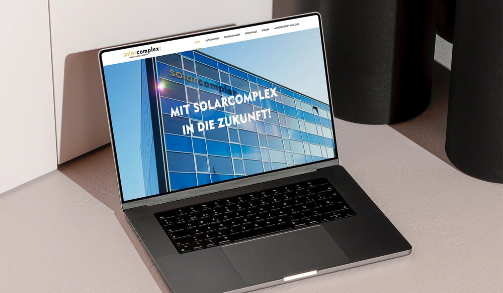Laptop-Mockup mit der Solarcomplex-Website, großen blauen Glastreppen und dem Tagline ‚MIT SOLARCOMPLEX IN DIE ZUKUNFT!'
